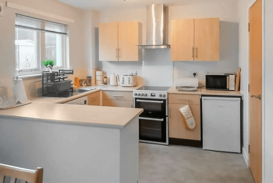 Kitchen at Beechwood with beech cabinets, electric oven and stainless extractor under a garden-facing window