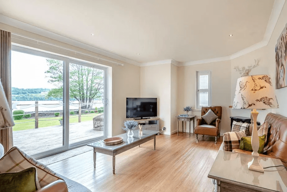 Living room with sliding doors framing Loch Lomond views from a leather sofa at Duck Bay Cottage 1