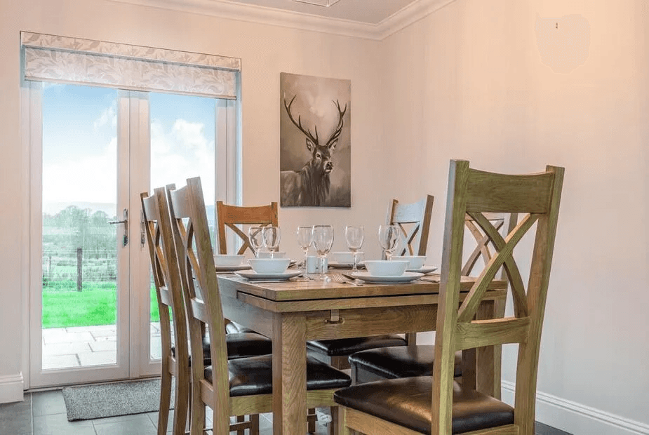 Dining at Fiadh Ruadh with oak table, six chairs and patio doors to the field with stag artwork