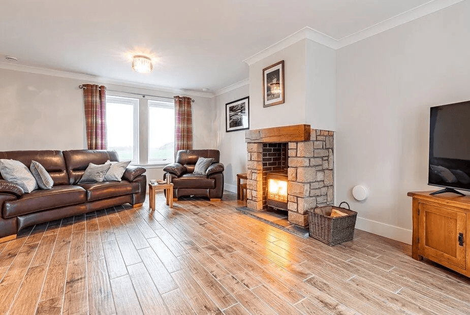 Lounge at Gartclach with leather sofa, lit wood-burner in stone surround and bay window to the field
