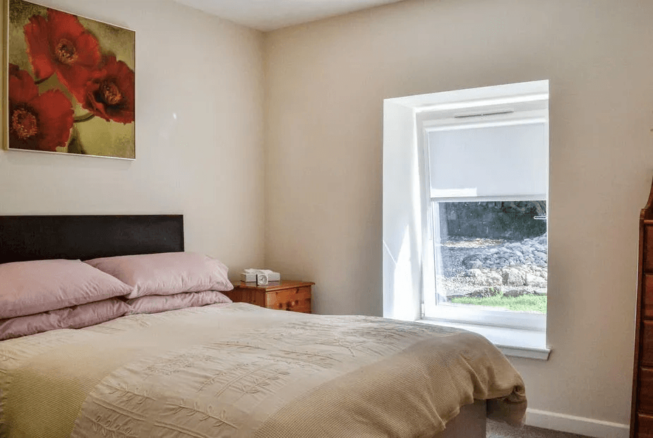 Bedroom at Holly Apartment with dark headboard, pink poppy artwork and beige bedding