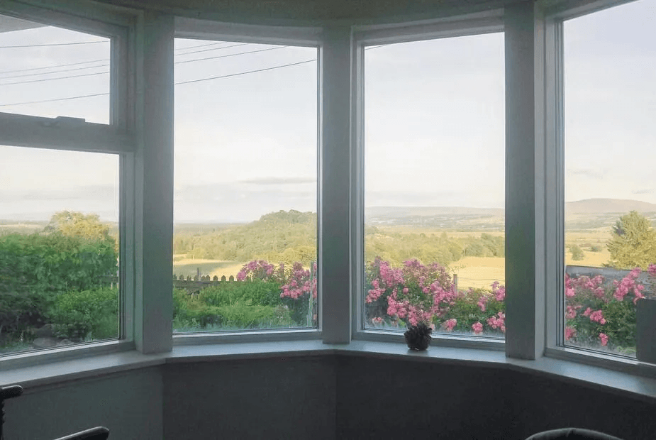 Bay window view across the Forth Valley with pink roses below at Puddingstone Cottage, Gartmore