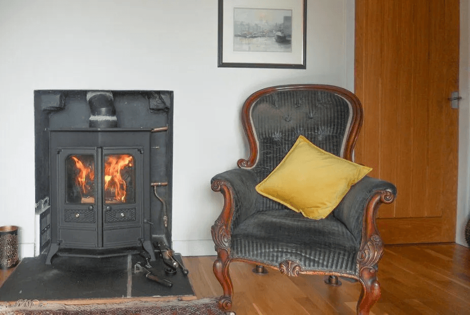 Lit wood-burning stove next to a velvet armchair at Puddingstone Cottage
