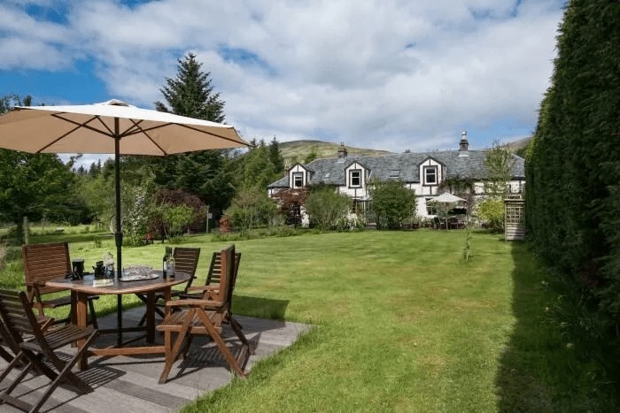 Strone House whitewashed country home with crow-stepped gables seen across the garden, dining table under a parasol, Garelochhead