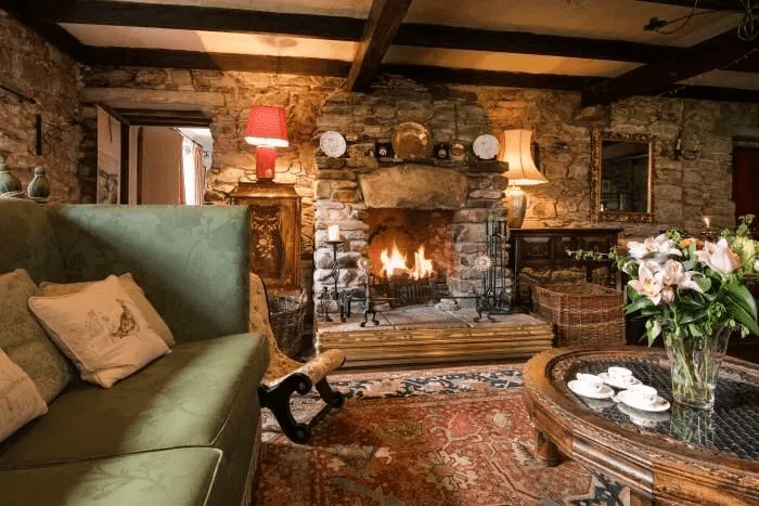 Beamed sitting room at Strone House with stone fireplace and roaring fire, green damask sofa and Persian rug