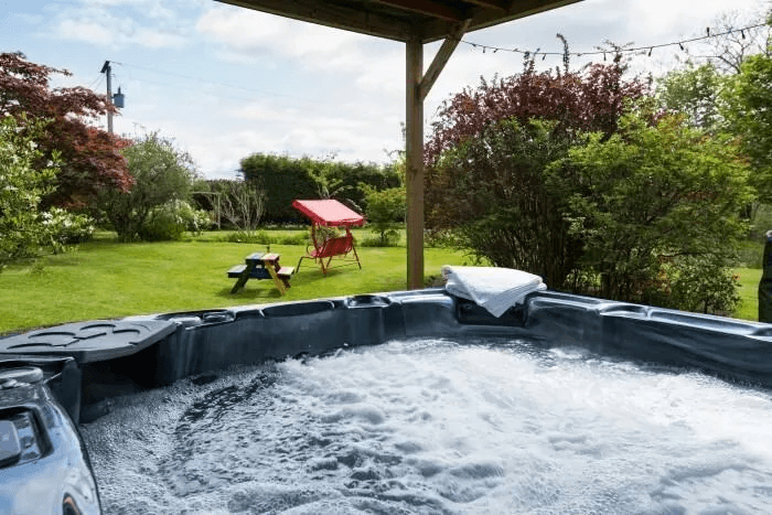 Outdoor hot tub at Strone House bubbling under a covered deck with garden, picnic table and shrubs beyond