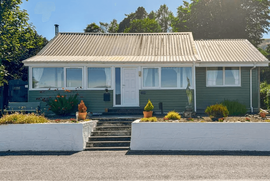 The Heron green-painted wooden cottage with corrugated metal roof, white door and stepped retaining wall, Dunoon