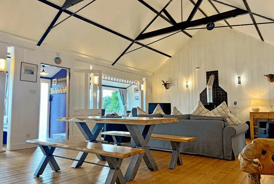 Vaulted open-plan living and dining at The Heron with exposed black beams, bench dining table and woodburner